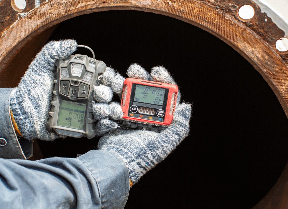 Operatore con guanti protettivi utilizza strumenti portatili per il monitoraggio della qualità dell’aria all’ingresso di un serbatoio industriale, in un contesto di sicurezza ambientale e servizi di noleggio strumentazione