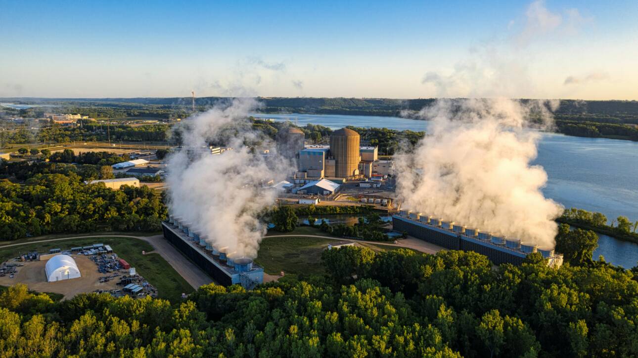 Panoramica aerea di un grande impianto industriale, una centrale nucleare con torri di raffreddamento attive, situata in un'area verde vicino a un fiume, a simboleggiare l'importanza della gestione delle emissioni industriali.